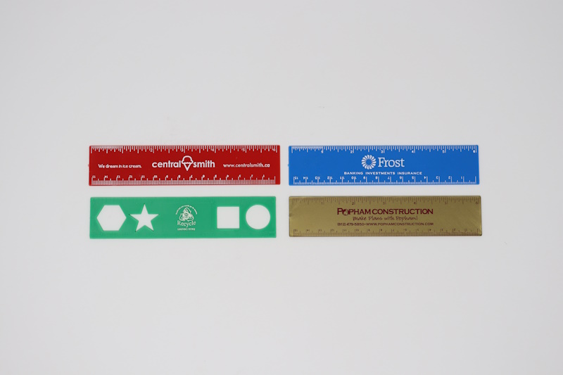 Red, blue, and gold plastic 6" rulers and green plastic 6" stencil ruler with imprints.